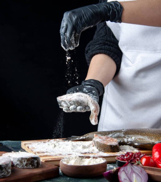 front-view-chef-covering-raw-fish-slices-with-flour-kitchen-table